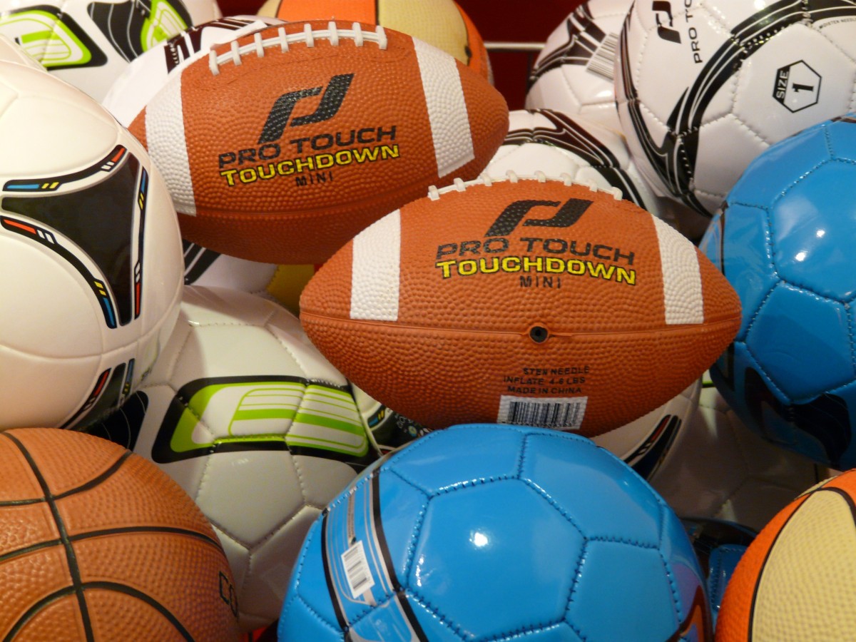Nærmynd af ýmsum íþróttaboltum, þar á meðal ruðningsboltum, knattspyrnuboltum og körfubolta, sem liggja saman í hrúgu.