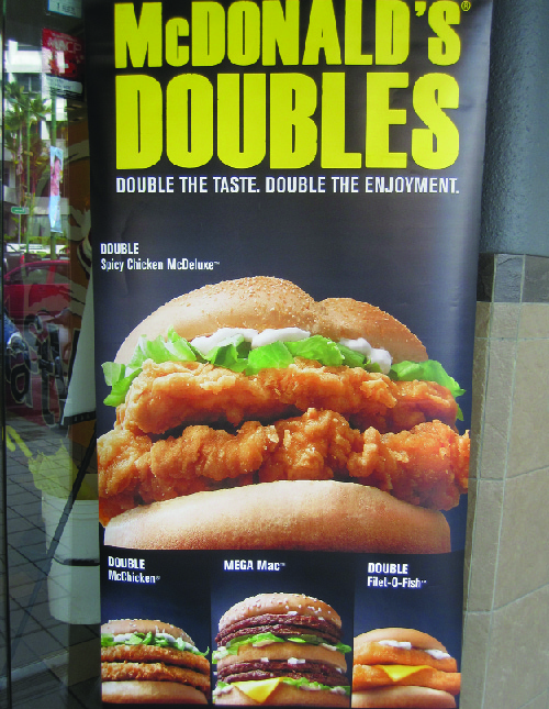 Myndin sýnir auglýsingu fyrir McDonald’s Doubles. Þar stendur: „Tvöfalt bragð. Tvöföld ánægja.“ Hún sýnir fjórar samlokur: Double Spicy Chicken McDeluxe, Double McChicken, Mega Mac og Double Filet-O-Fish.