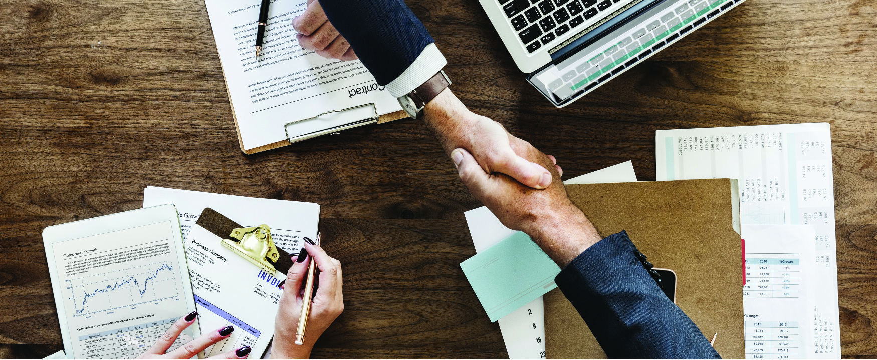 Tvær manneskjur takast í hendur yfir viðarborði.