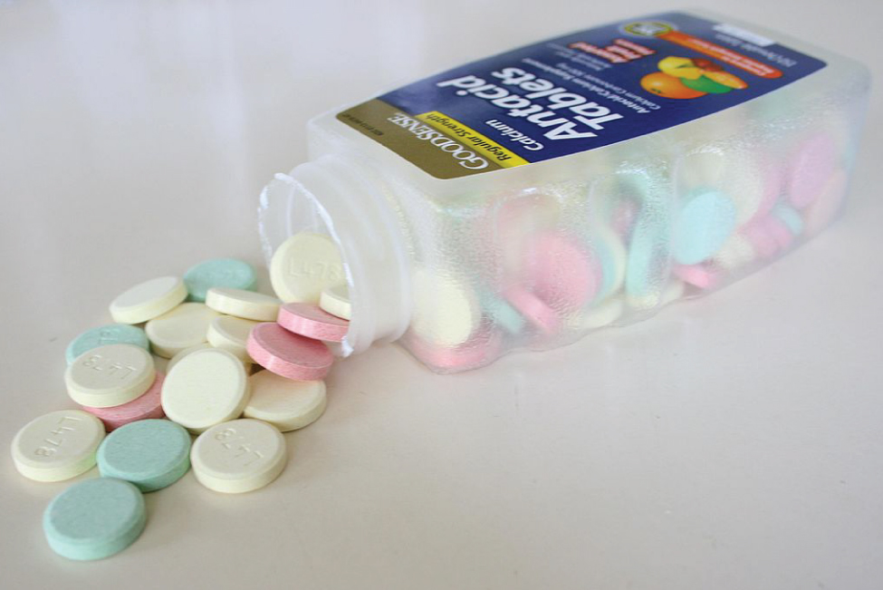 Ljósmynd sýnir flösku sem liggur á hliðinni með orðunum „Antacid Tablets“ skrifuðum framan á. Fjöldi litríkra, fastra taflna hellist út úr opi flöskunnar.
