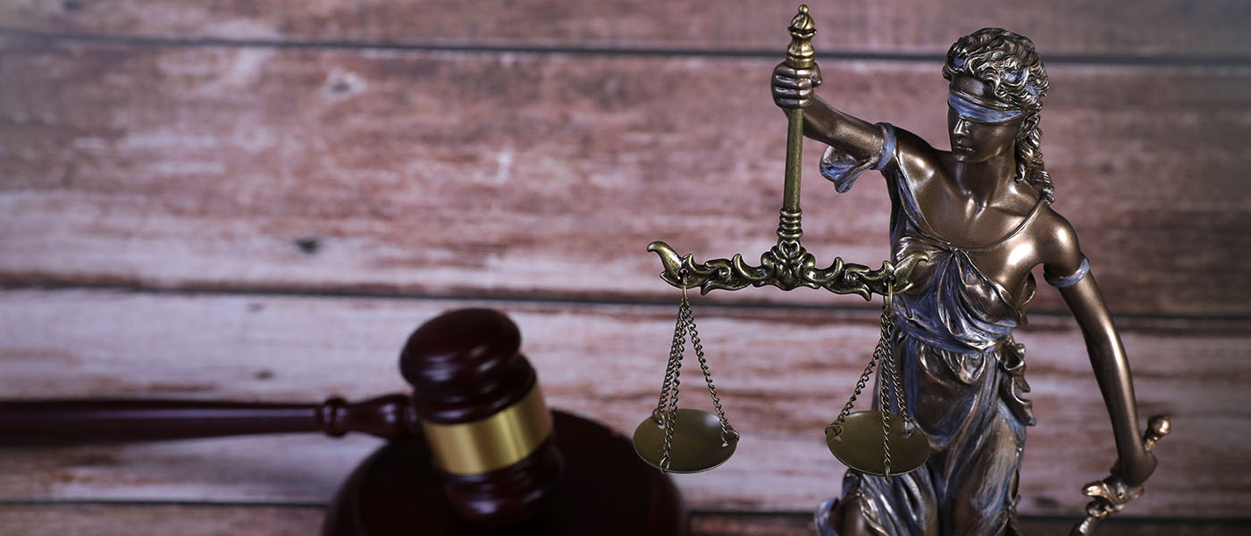 Bronsstytta af Justitiu, gyðju réttlætisins, sem heldur á sverði og vog; dómarahamar sést í bakgrunni.