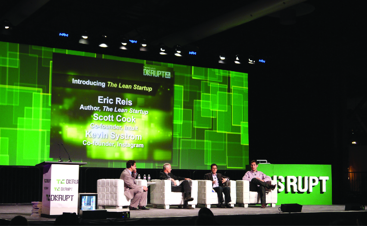 Fjórir karlmenn sitja á sviði og ræða Lean Startup-aðferðina. Á skjá sjást nöfnin Eric Ries (höfundur The Lean Startup), Scott Cook (meðstofnandi Intuit) og Kevin Systrom (meðstofnandi Instagram).