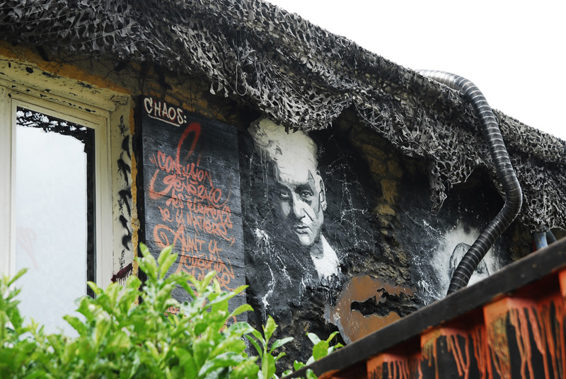 Málverk af Jacques Derrida á byggingu ásamt öðru veggjalistaverki.