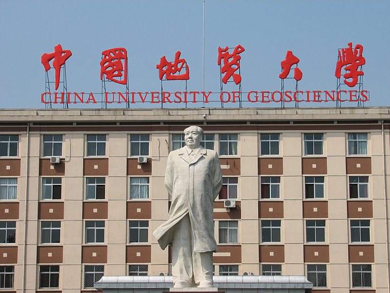 Stytta af Maó formanni fyrir framan stóra nútímabyggingu með skilti á kínversku og ensku. Enski textinn er „China University of Geosciences“.