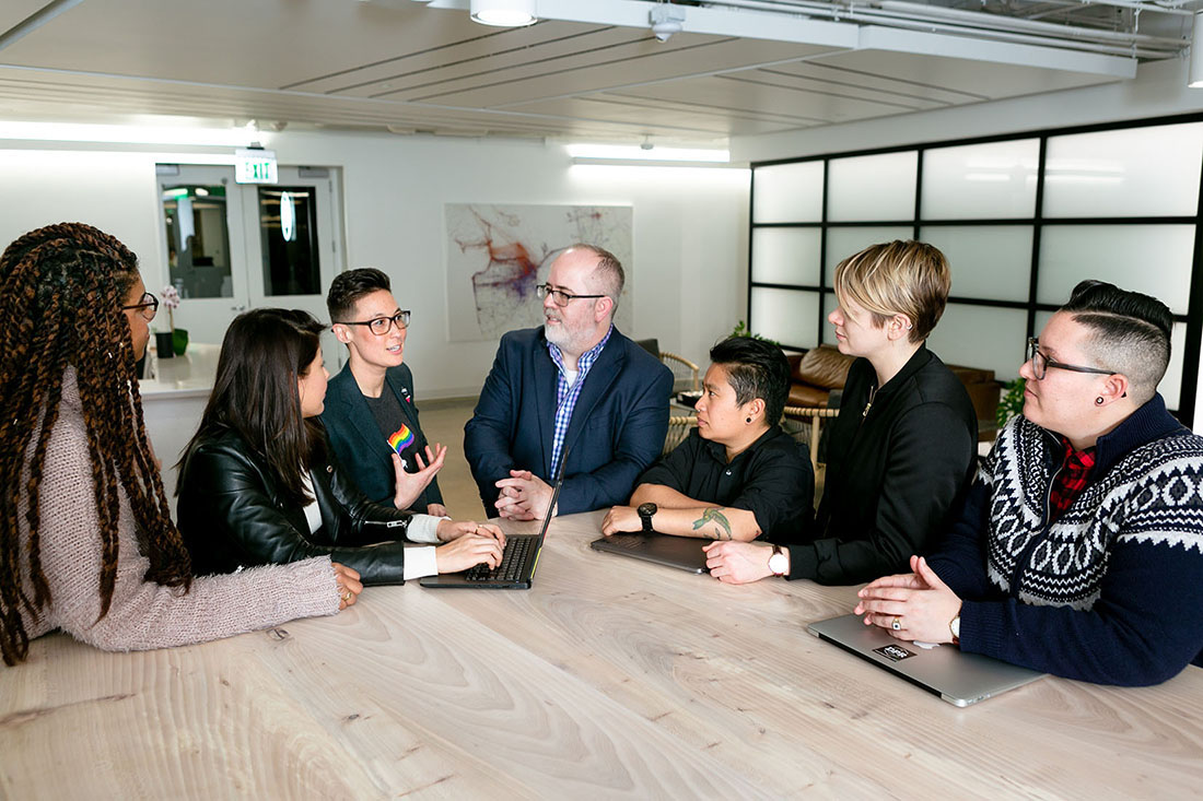Sjö manneskjur standa kringum fundarborð.