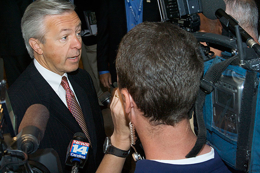 John Stumpf, forstjóri Wells Fargo, ræðir við fréttamenn sem þyrpast að honum með hljóðnema og myndavélar.
