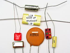 This is a photograph showing seven small capacitors, of varying shapes and colors, usually found in electronic circuits.