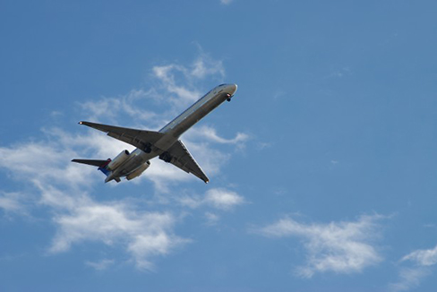 A photograph of an airplane flying in an upward direction is shown. The sky is partly cloudy.