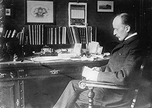 Ljósmynd af Max Planck þar sem hann situr við skrifborð og les skjal.