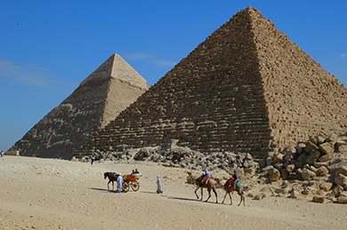 Ljósmynd af fólki á úlföldum fyrir framan tvo píramída í Egyptalandi.
