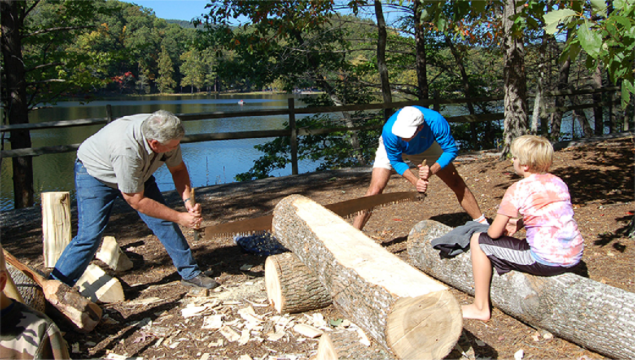 Tveir menn saga trjábol með tveggja manna þversög utandyra meðan barn fylgist með.