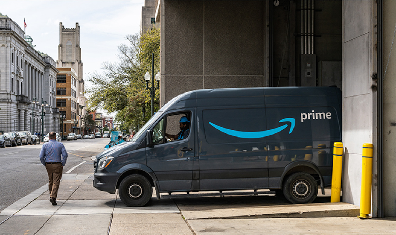 Prime-sendibíll Amazon stendur við vörumóttöku í borgargötu.