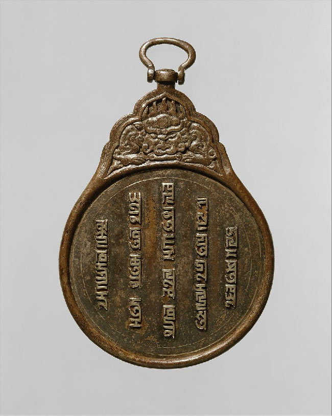 Á gráum grunni sést gljáandi brún plata. Neðri hluti hennar er kringlóttur en efst er oddmjótt skraut og lykkja á hjörum. Á neðri hlutanum er forn áletrun í dálkum. Skrautið efst líkist stóru skrímslishöfði með víðar nasir, gildar framlimi, stórar hendur og horn.