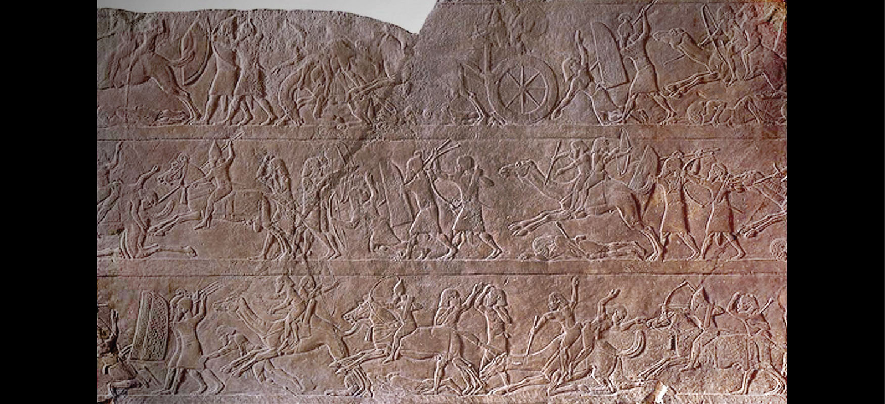 Myndin sýnir brúnan stein með útskornum bardagaatriðum í þremur röðum. Efsti hluti steinsins er brotinn vinstra megin og sprunga liggur niður eftir miðjum steininum. Atriðin sýna fólk í bardaga. Fólkið er í klæðum sem bundin eru um mittið, ber íburðarmikinn höfuðbúnað og notar skildi sér til varnar. Sumir berjast með spjótum, sverðum, bogum og örvum og aðrir ríða úlföldum og hestum eða aka stríðsvögnum. Sumir liggja á jörðinni eða falla.