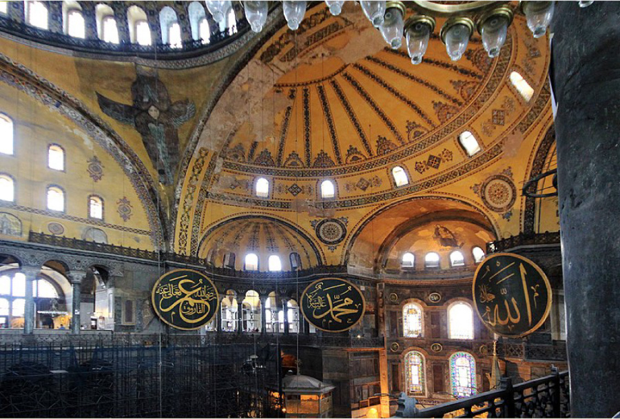 Ljósmyndin sýnir Hagia Sophia að innan. Í byggingunni eru ríkulega skreytt hvolfþök. Á veggjunum hanga stórar skífur með arabískri áletrun.