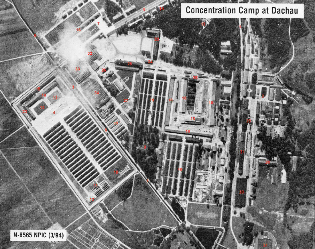 Þetta er svarthvít loftmynd með heitinu „Fangabúðirnar í Dachau“. Önnur áletrun er „N-6565 NPIC (3/94)“. Efst fyrir miðju er stór trjáþyrping og minni trjáreitir eru á víð og dreif hægra megin og fyrir miðju. Vinstra megin á myndinni eru tvær skipulegar raðir af löngum, mjóum byggingum og opið svæði. Vegir og gangstéttir liggja um myndina.